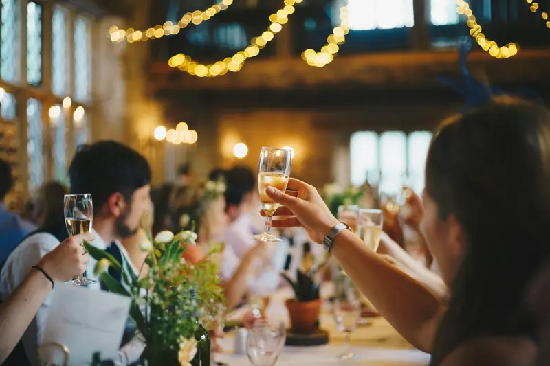 Invitados levantan sus copas en un brindis durante una cena, bajo guirnaldas de luces cálidas